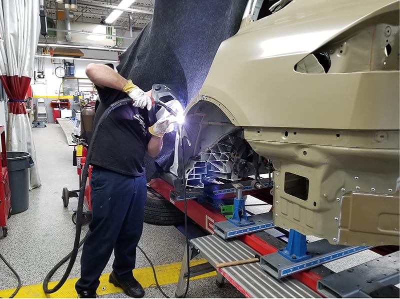 Technician at a certified collision center repairing a luxury automobile.