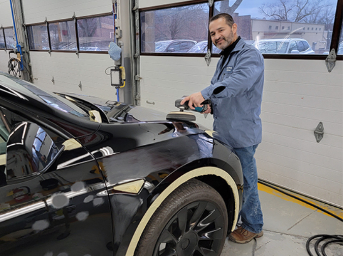 Man working on a black car in a garage, smiling.